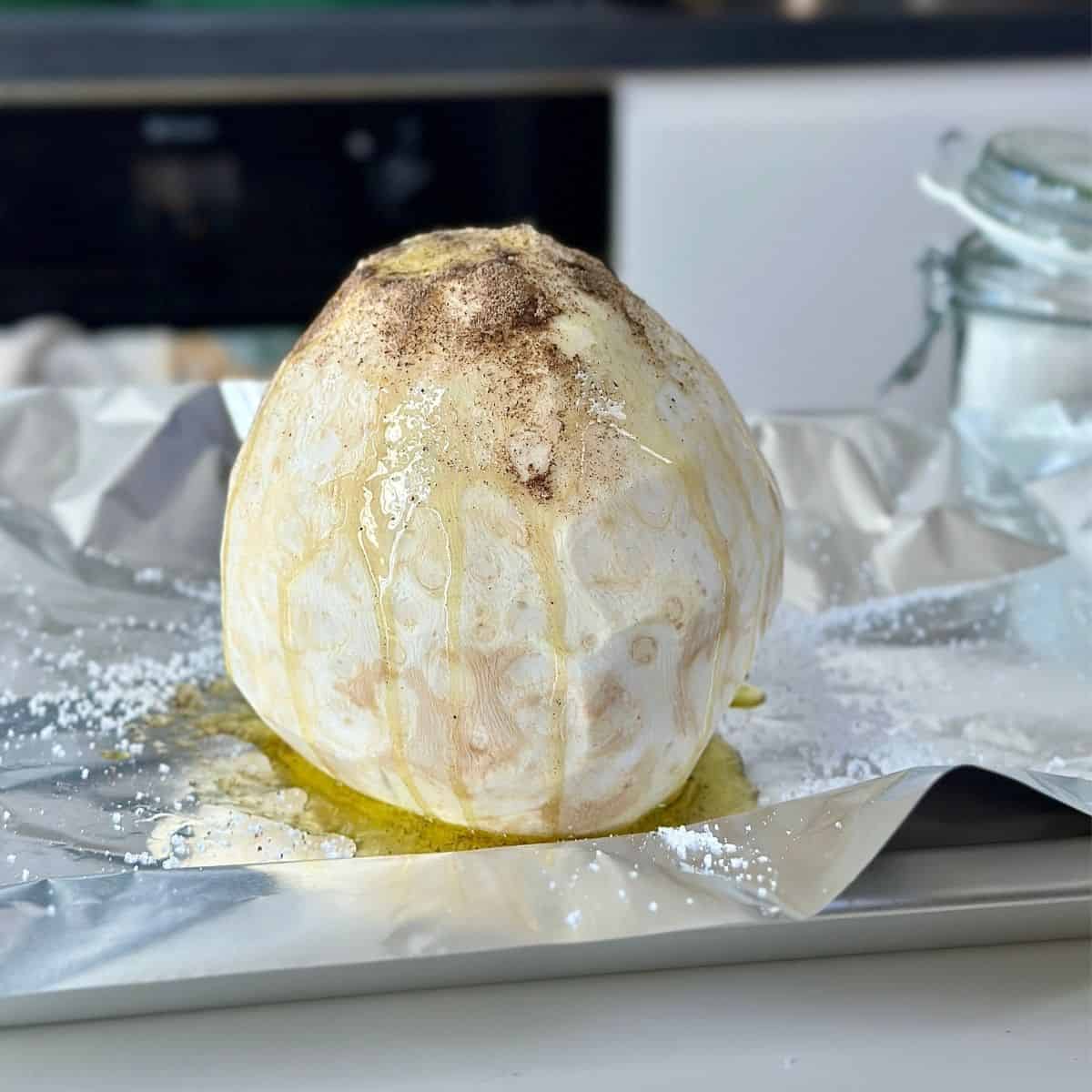 A whole, peeled celeriac coated in olive oil, salt and pepper, sitting on tin foil.