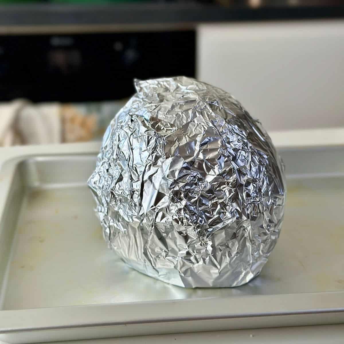 A whole celeriac wrapped in tin foil, sitting on a baking tray ready for roasting.