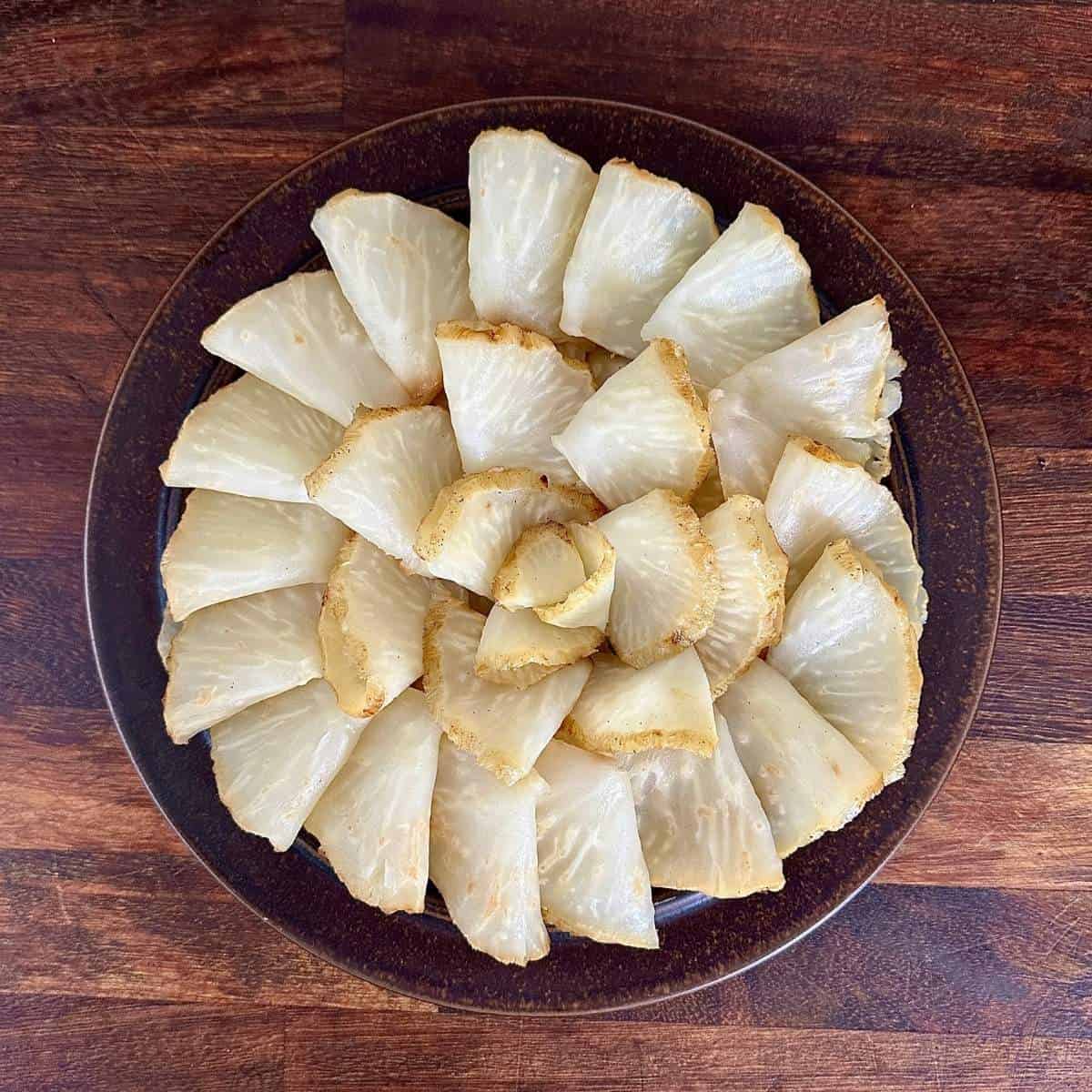 A brown plate contacting thin roasted celeriac half moon slices arranged in a circular shape.