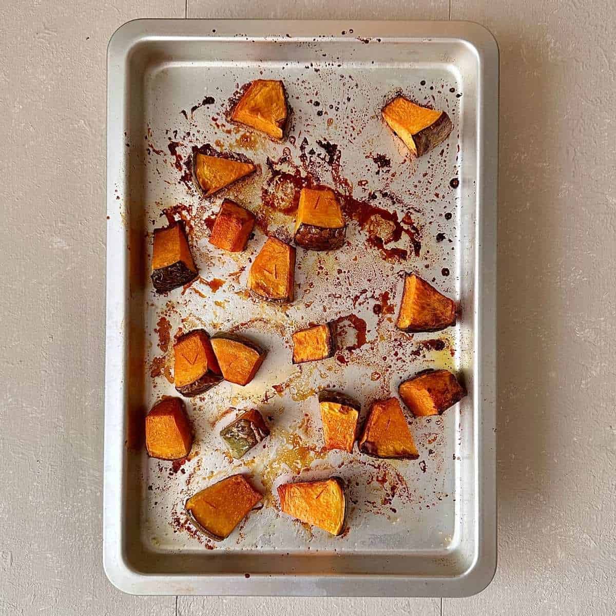 A baking tray with large chunks roasted crown prince pumpkin coated in sesame oil, mirin, salt and pepper for veggie ramen recipe.