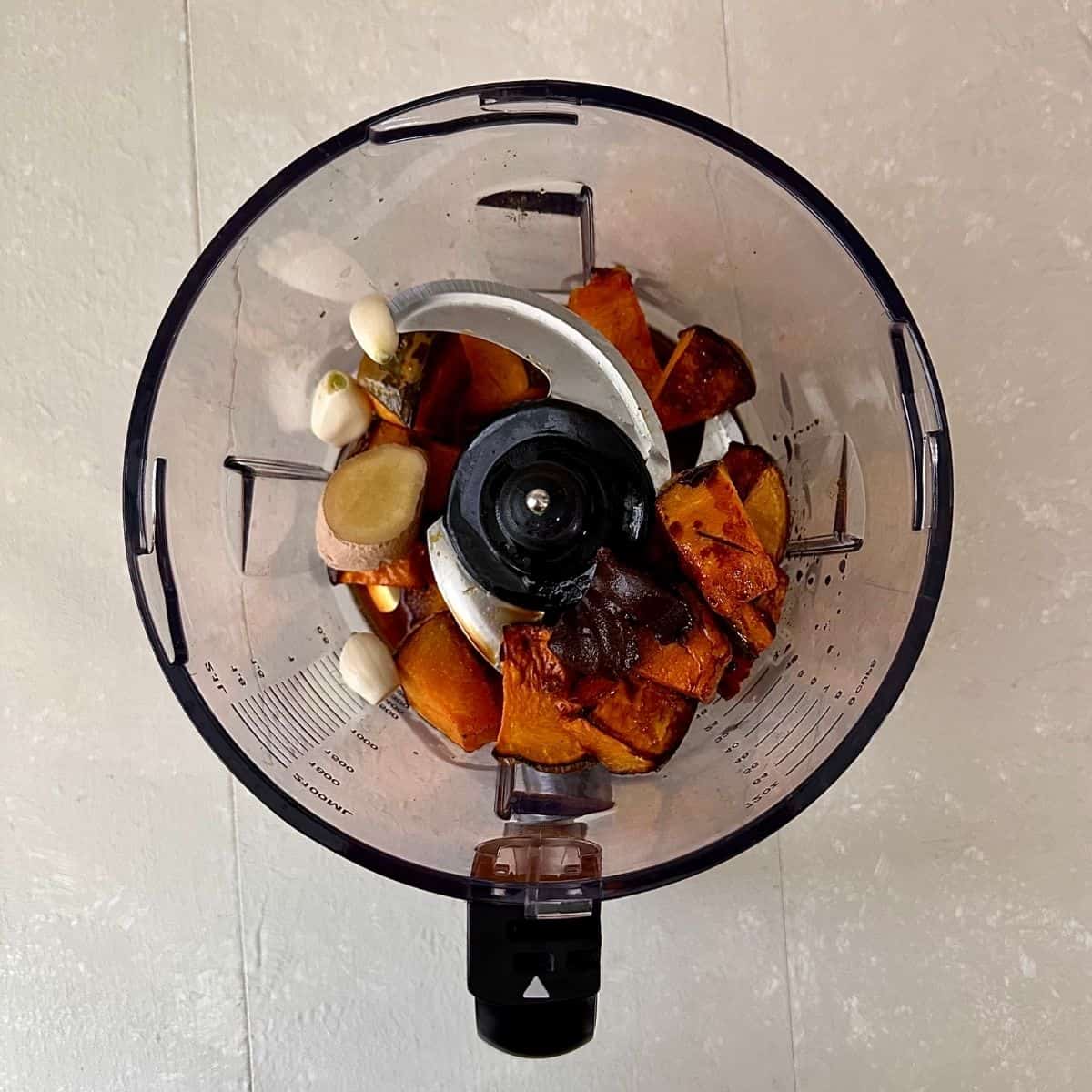 A large food processor jug containing chopped, roasted crown prince pumpkin, garlic, ginger and miso for veggie ramen recipe, ready to blend.