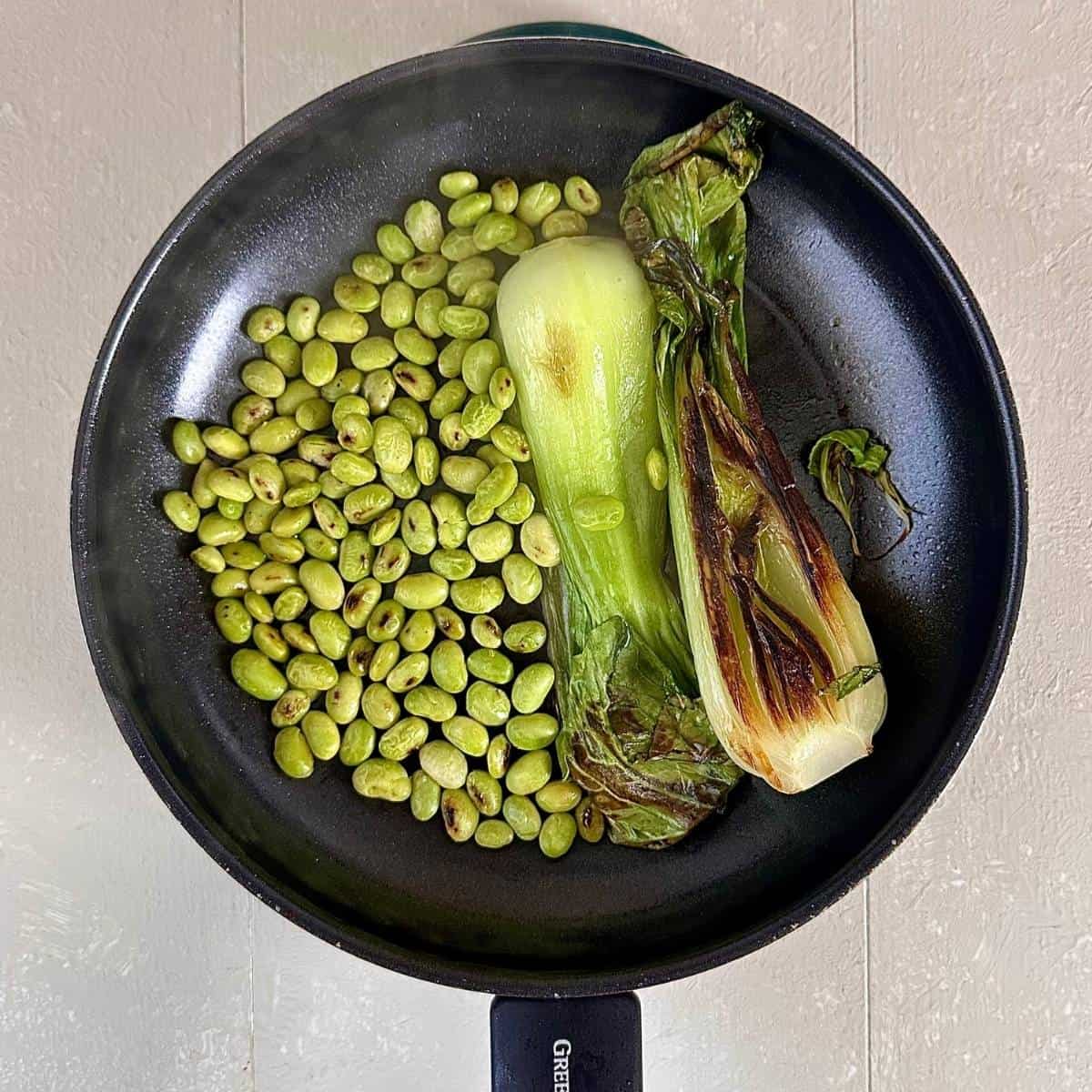 A frying pan containing slightly browned bok choy and edamame for veggie ramen garnish.