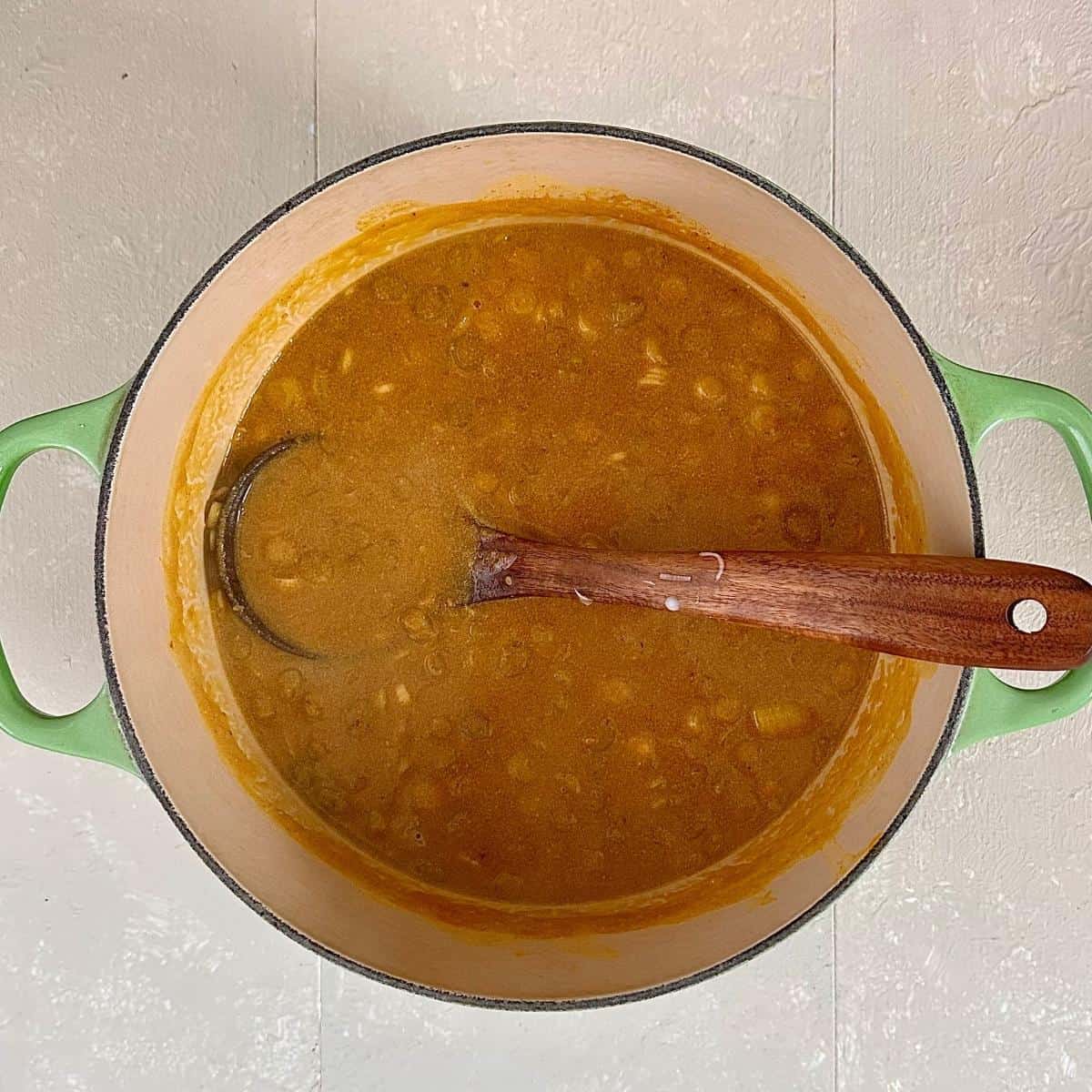 A large green saucepan containing pumpkin broth for veggie ramen recipe. A wooden spoon sits in the saucepan.