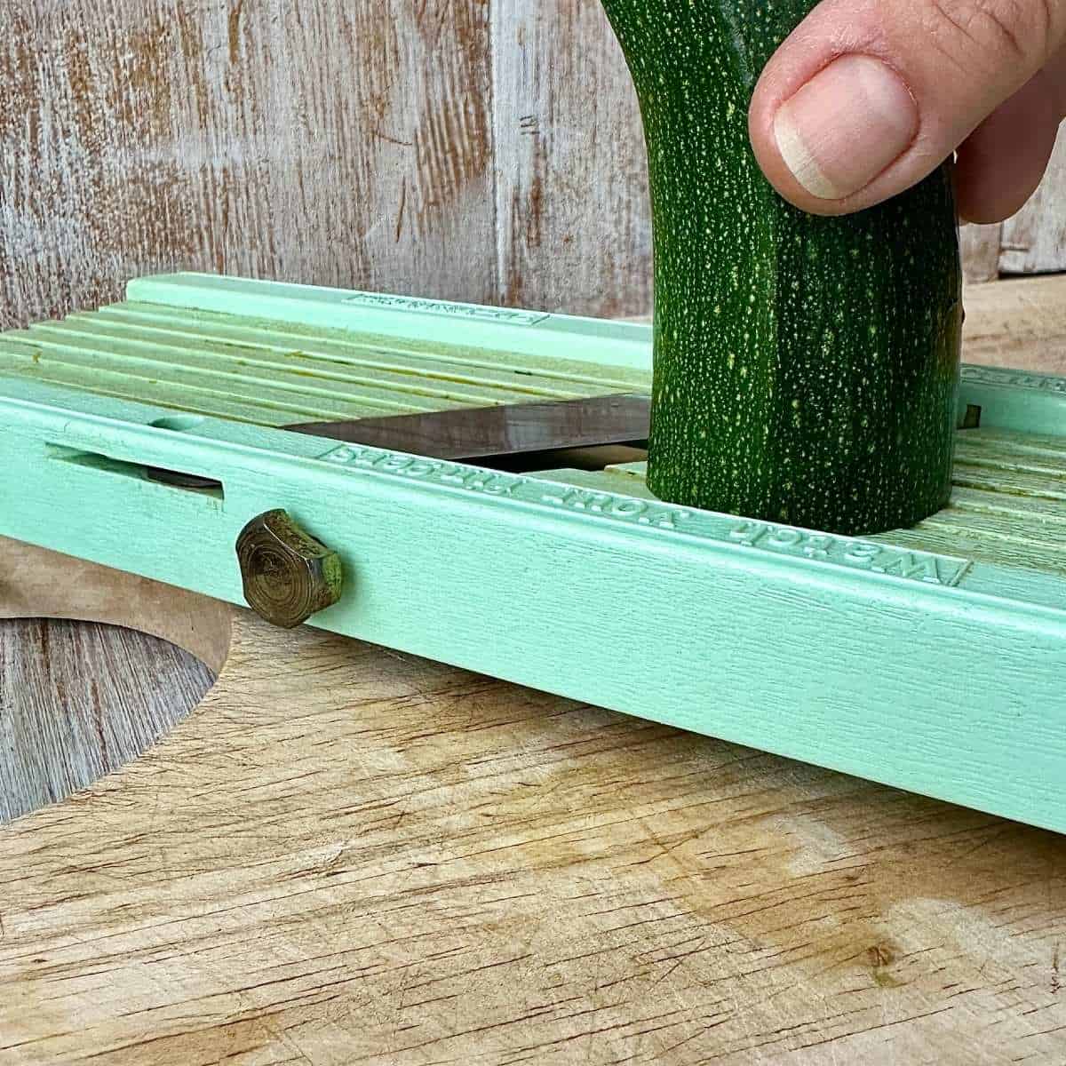 A courgette being held on a mandolin slicer just before the blade, ready to slice.