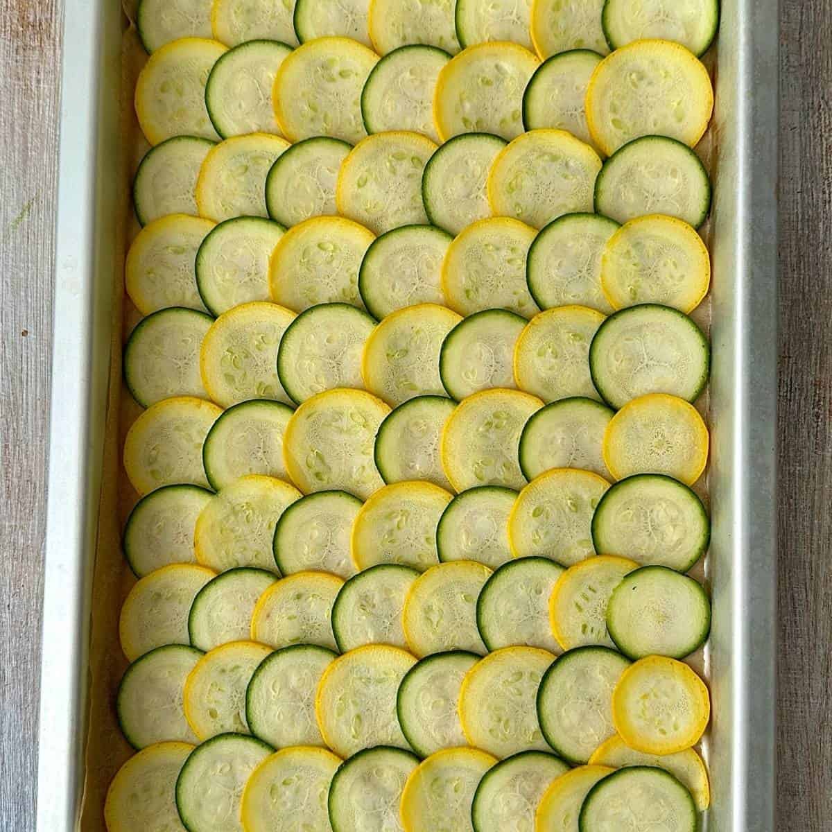 A parchment paper lined baking tray containing thinly sliced courgette discs, overlapping each other, ready to bake. For cottage cheese wraps with a courgette base.