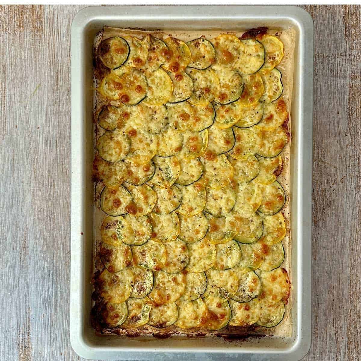 A baking tray containing a wrap sheet made with thinly sliced courgette and melted mozzarella and cheddar cheese, baked to a golden brown colour. For a cottage cheese wrap with a courgette base.