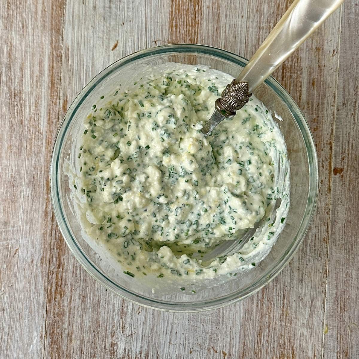 A glass bowl containing cottage cheese mixed with chives, salt, pepper and lemon juice. The filling for Cottage Cheese Wraps.