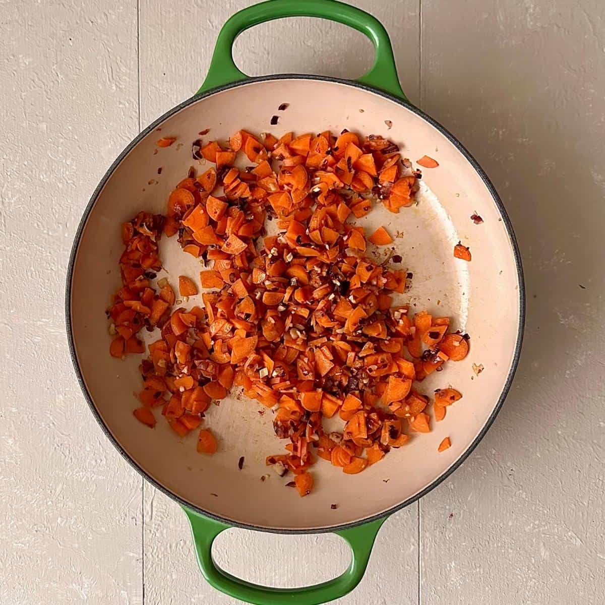 A shallow large green pot with fried chopped carrots, red onion and garlic for kimchi white bean stew.
