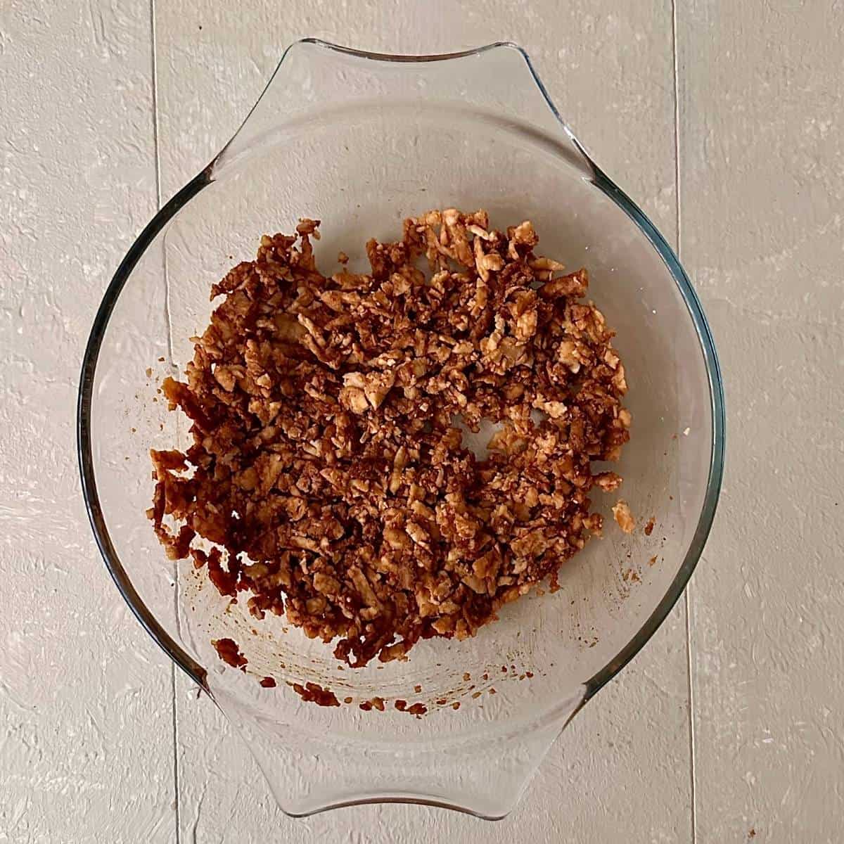 A glass bowl containing grated tempeh marinated with soya sauce and kimchi juice.