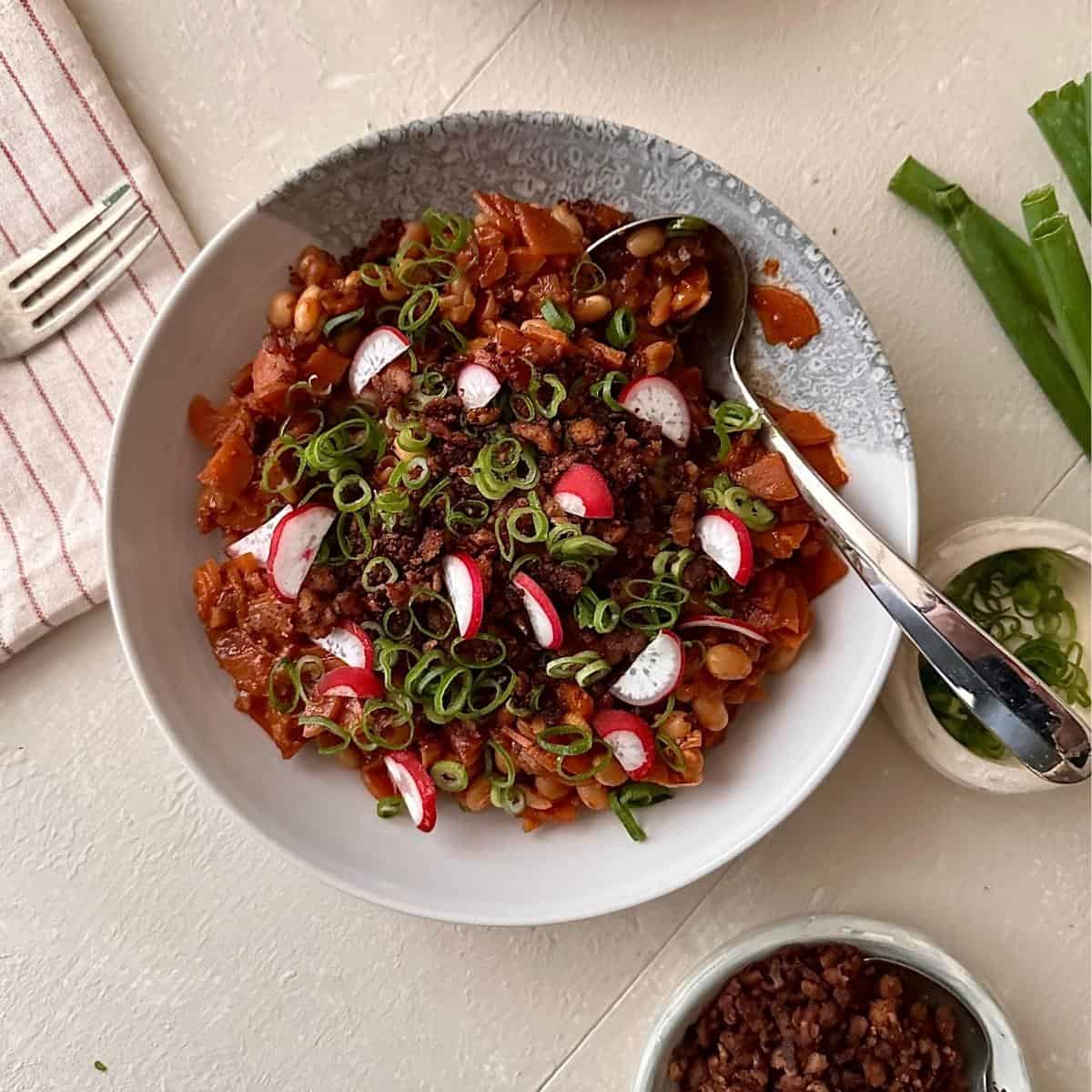 Kimchi white bean stew garnished with spring onion and sliced radish. A silver spoon sits in the bowl.