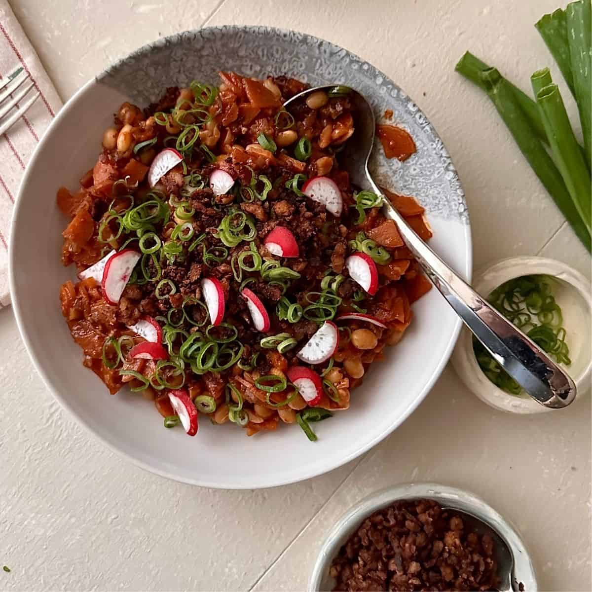 Kimchi white bean stew with tempeh crumble, radishes and spring onions in a bowl, viewed from above.