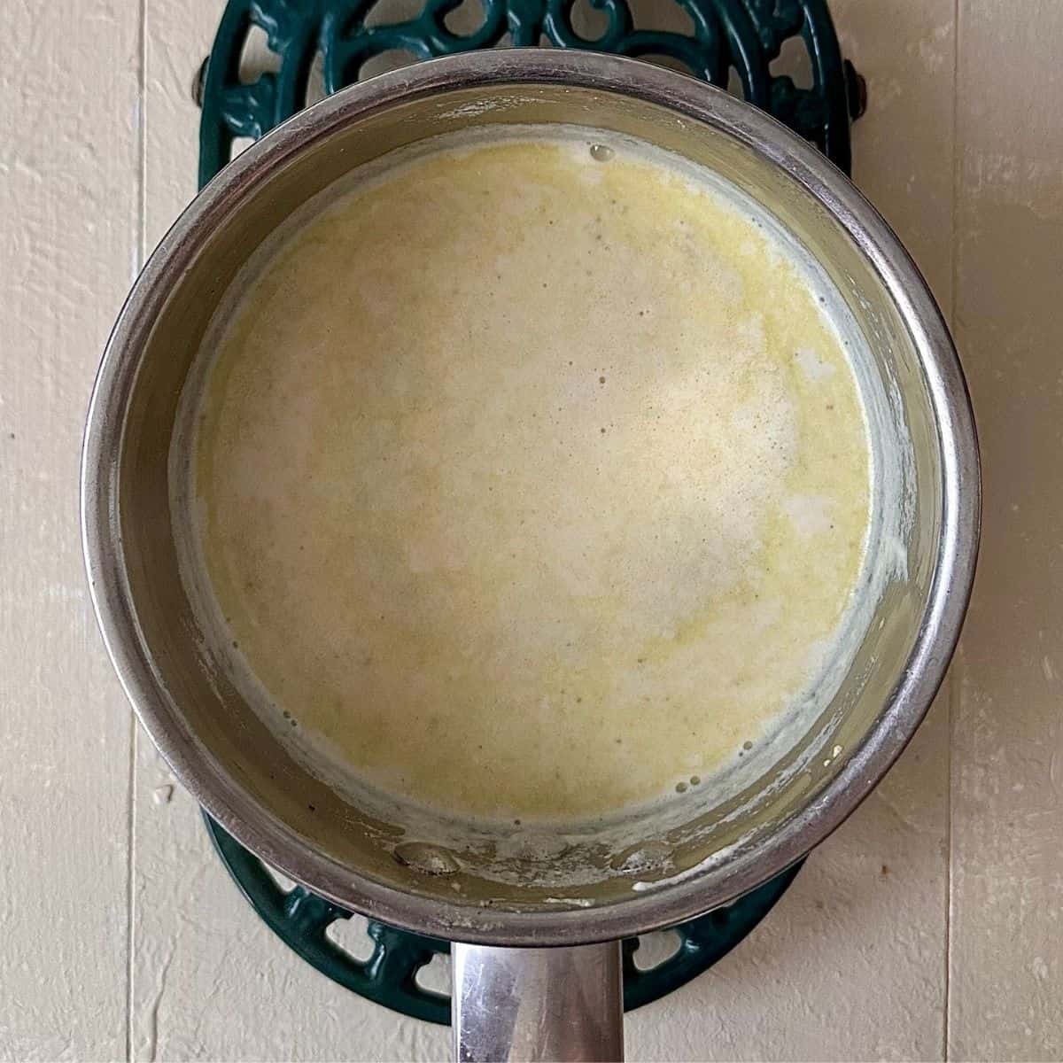 A saucepan containing milk, with dissolved castor sugar and thundai mix for no-bake thundai cream cake recipe.