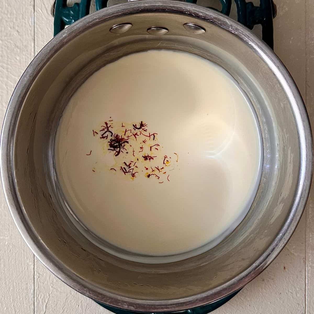 A saucepan containing cream with saffron in it. For a no-bake thundai cream cake.