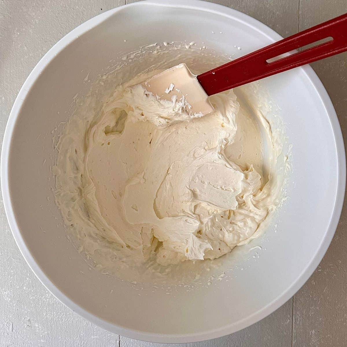 A white bowl containing mascarpone cheese, icing sugar and double cream whisked to soft peaks, for no-bake thundai cream cake.