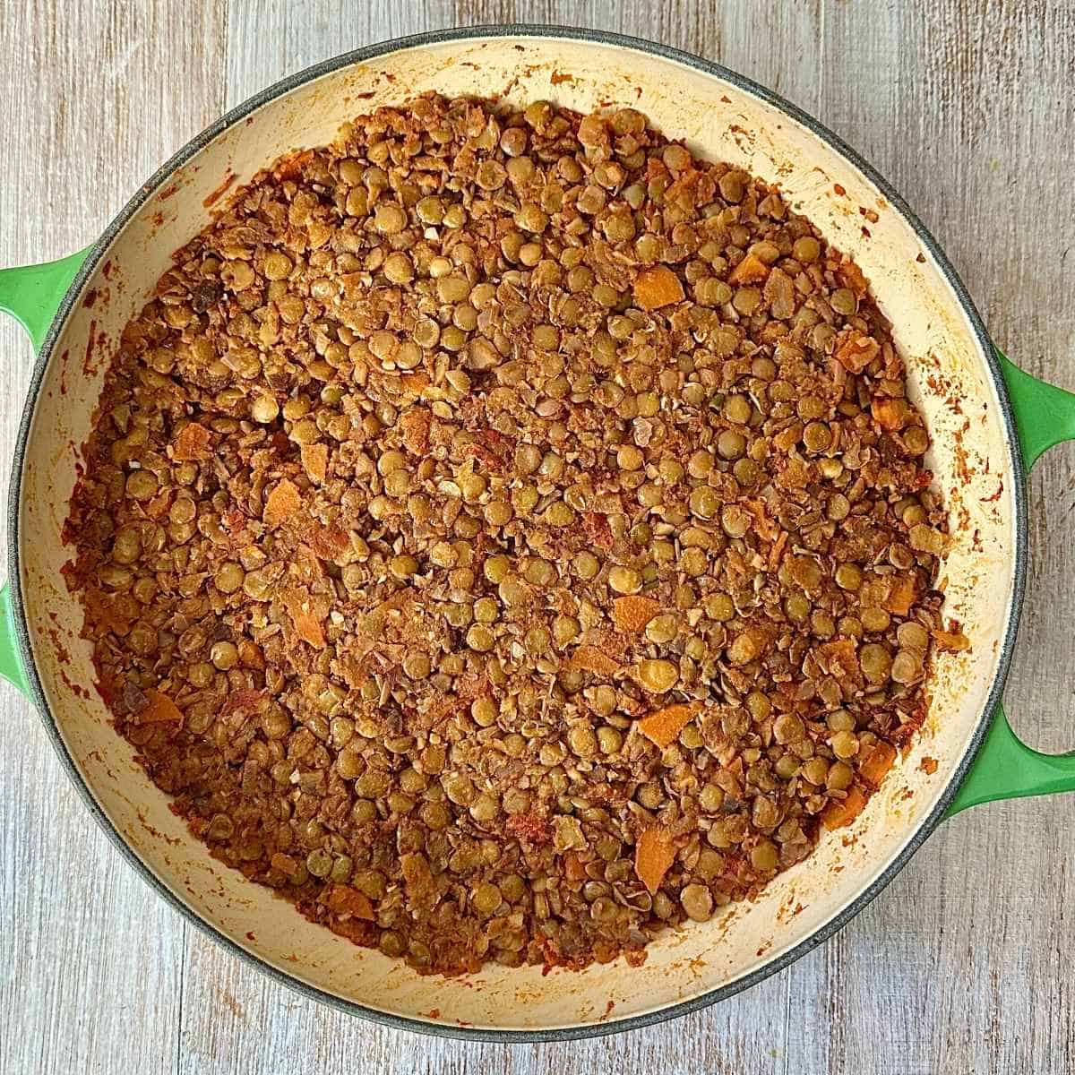 The cooked spiced lentil filling for a sweet potato lentil shepherds pie in a large green casserole dish.