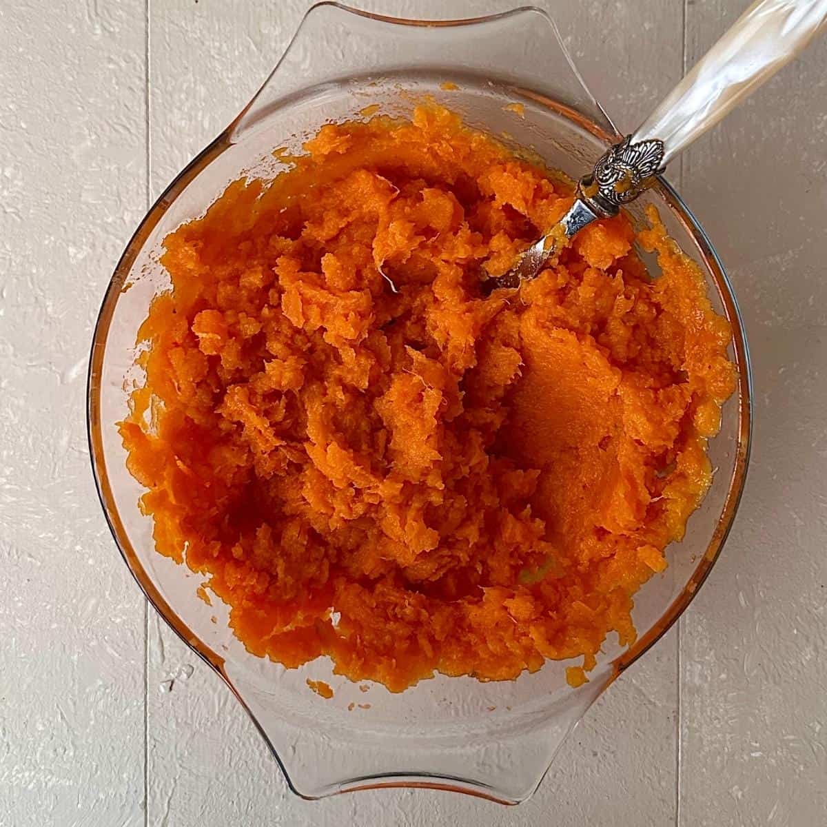 A glass dish containing mashed sweet potato for sweet potato shepherd's pie.