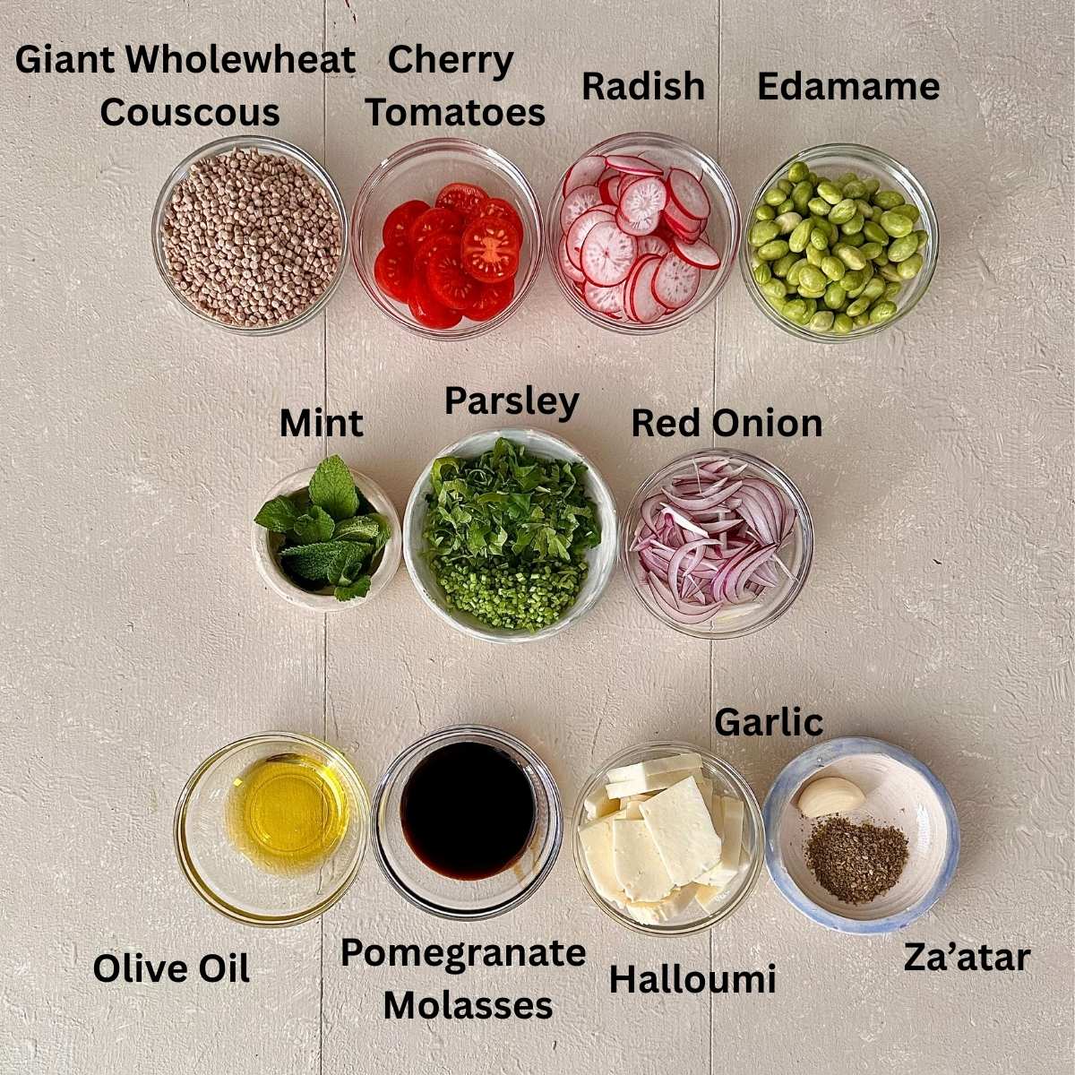 Prepared ingredients for za'atar halloumi couscous salad in small glass dishes. The ingredients are annotated.