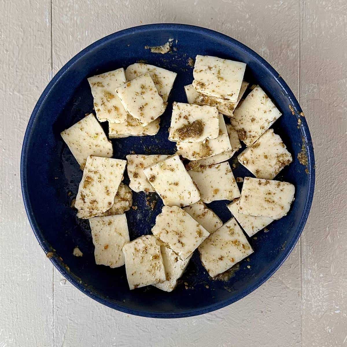 A blue bowl containing halloumi pieces marinated with olive oil a za'atar for za'atar halloumi couscous salad.