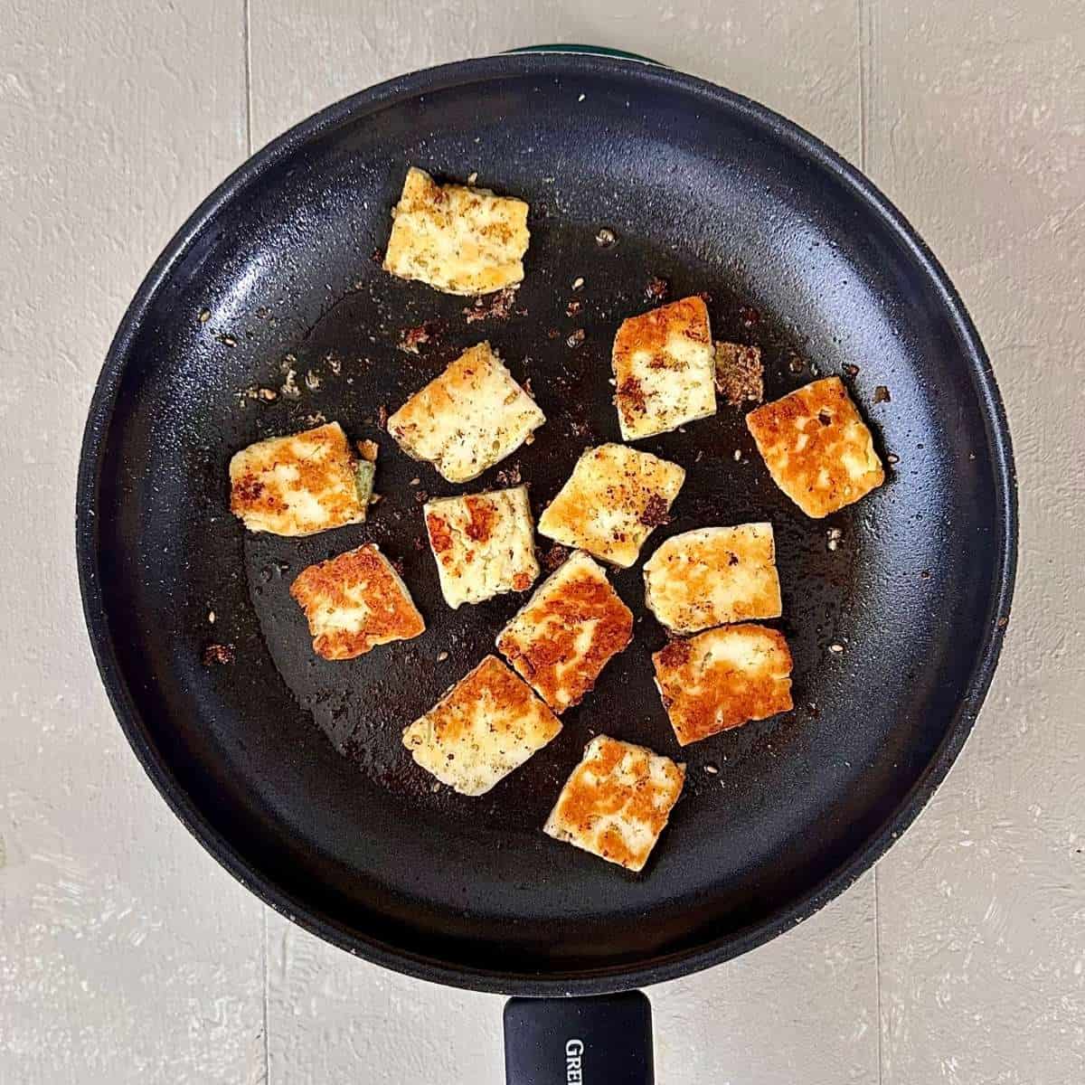 A frying pan contain fried golden pieces of halloumi for za'atar halloumi couscous salad.