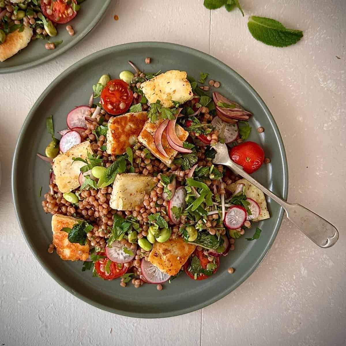 A green plate with za'atar halloumi couscous salad garnished with parsley and mint.