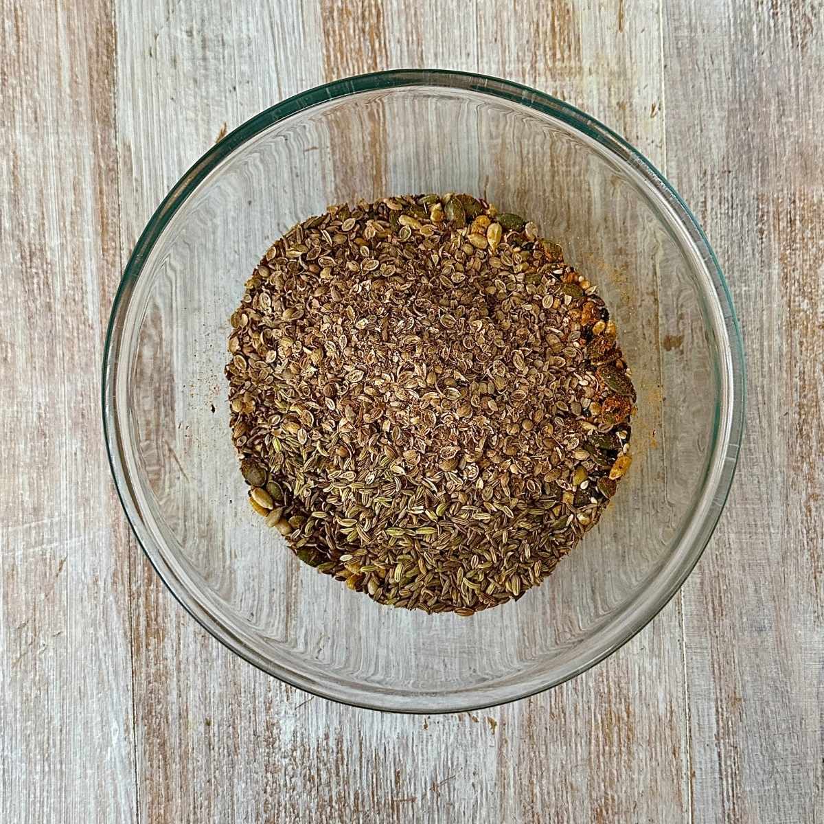 A glass bowl containing mixed toasted seeds and spices and turmeric.