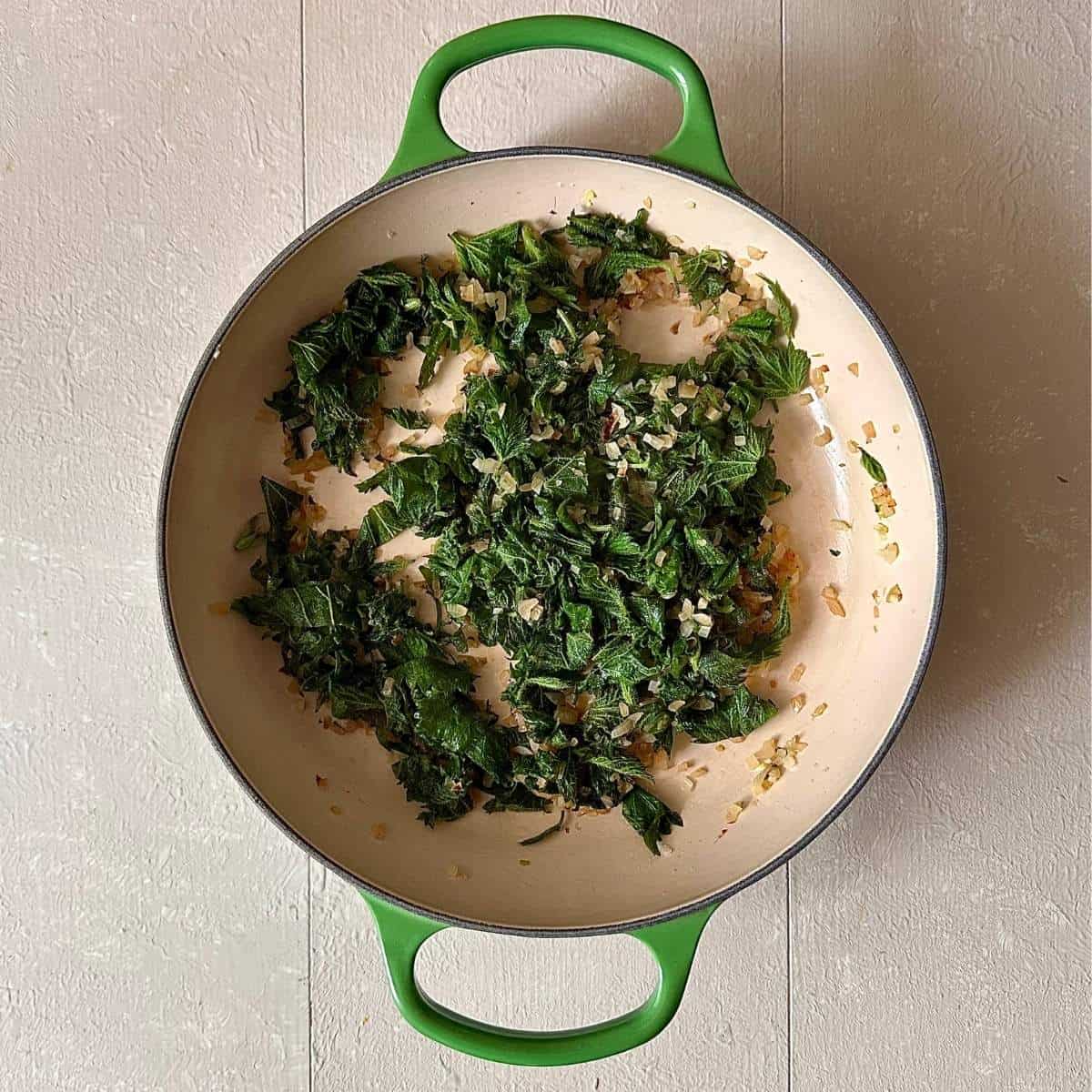 A large green casserole contains finely chopped fried onion and fried nettle leaves for wild garlic and nettle cauliflower cheese.