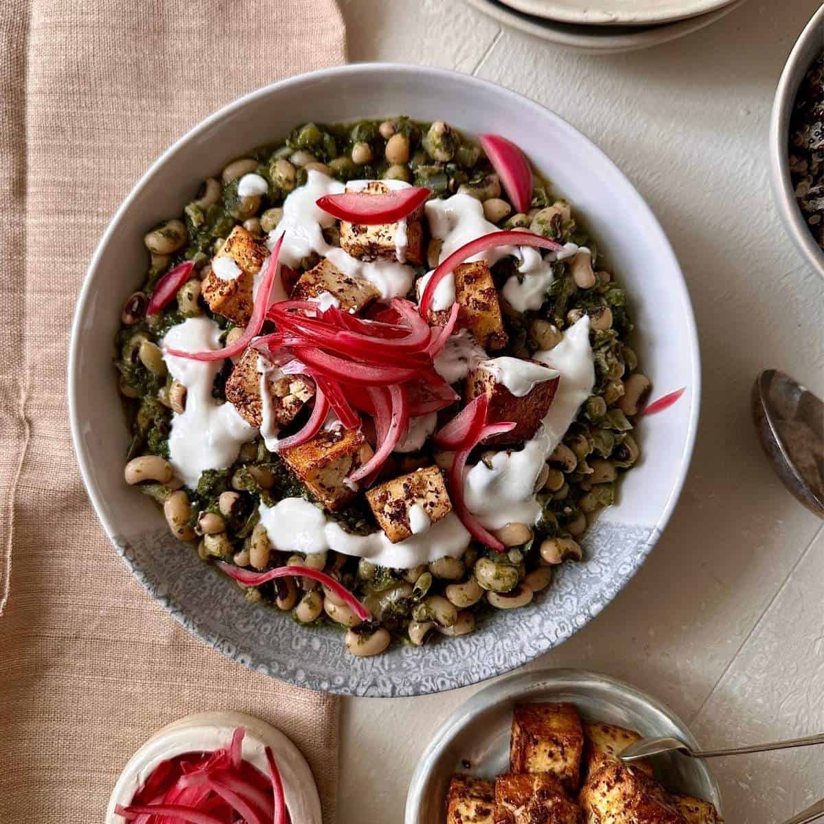 Black eyed peas with smoked tofu, tahini yoghurt and pickled red onion in a white serving bowl.