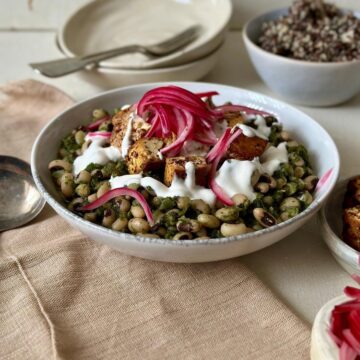 Black eyed peas with smoked tofu topped with tahini yoghurt and pickled red onion in a white serving bowl.