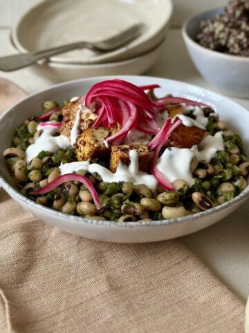 Black eyed peas with smoked tofu topped with tahini yoghurt and pickled red onion in a white serving bowl.