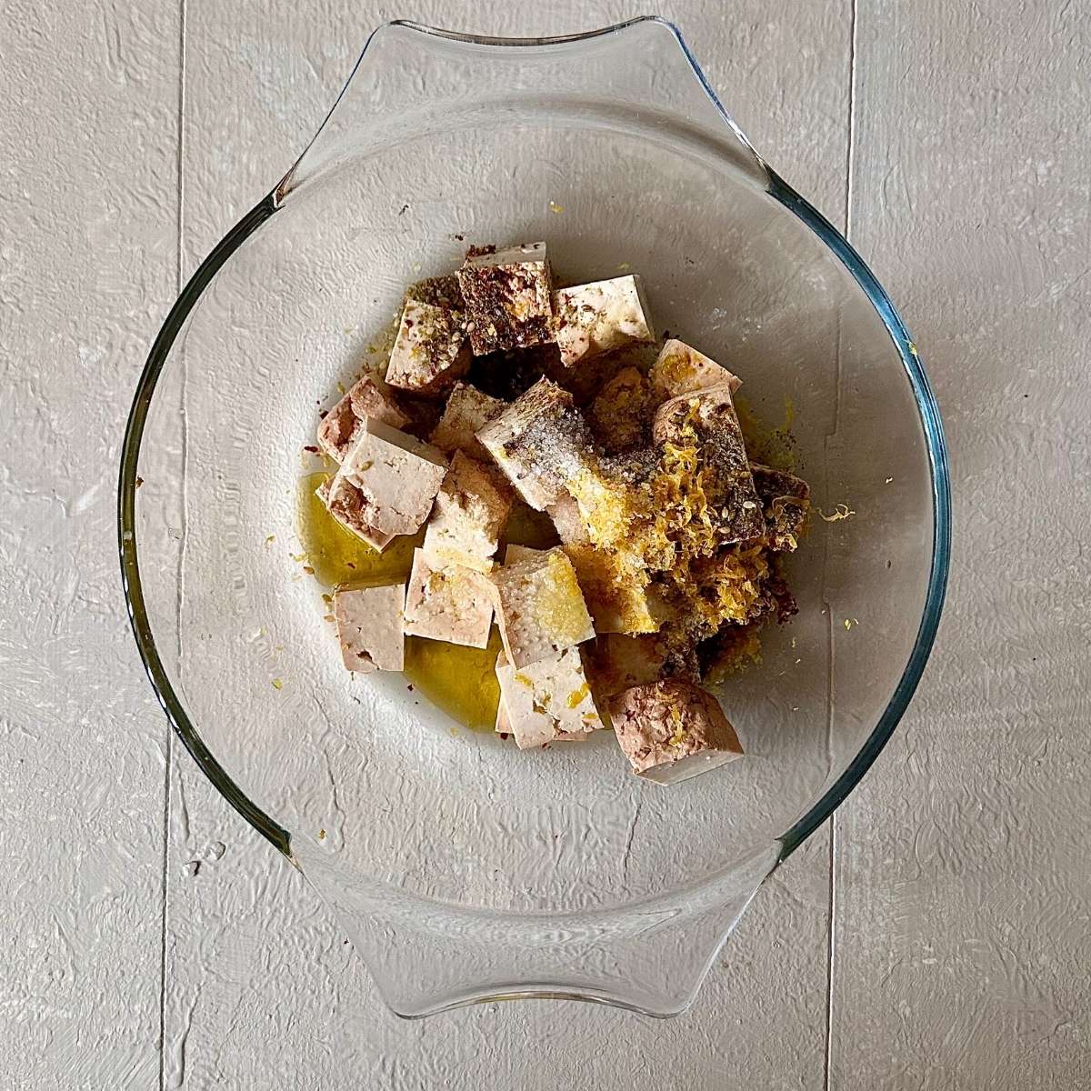 A glass bowl contains cubes of smoked tofu with a za'atar and allepo pepper marinade for black eyed peas with smoked tofu recipe.