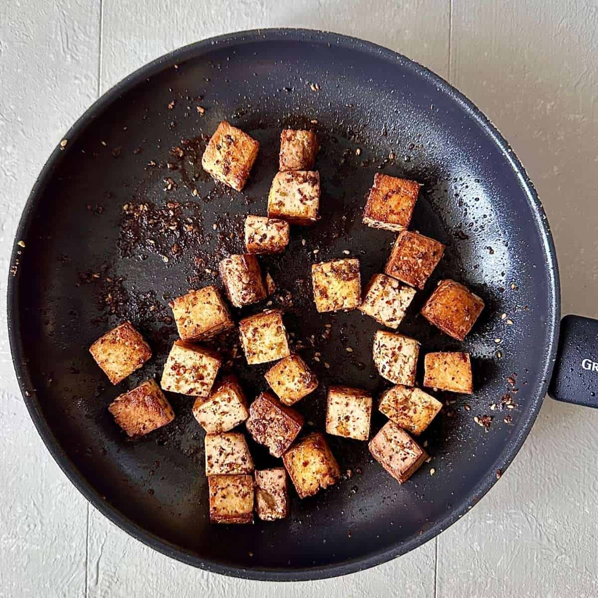 A large frying pan containing cubes of fried smoke tofu for black eyed peas with smoked tofu