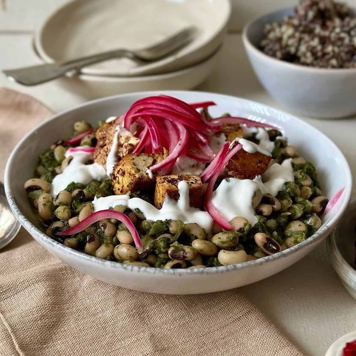 Black eyed peas with smoked tofu topped with tahini yogurt and pickled red onion in a white bowl.