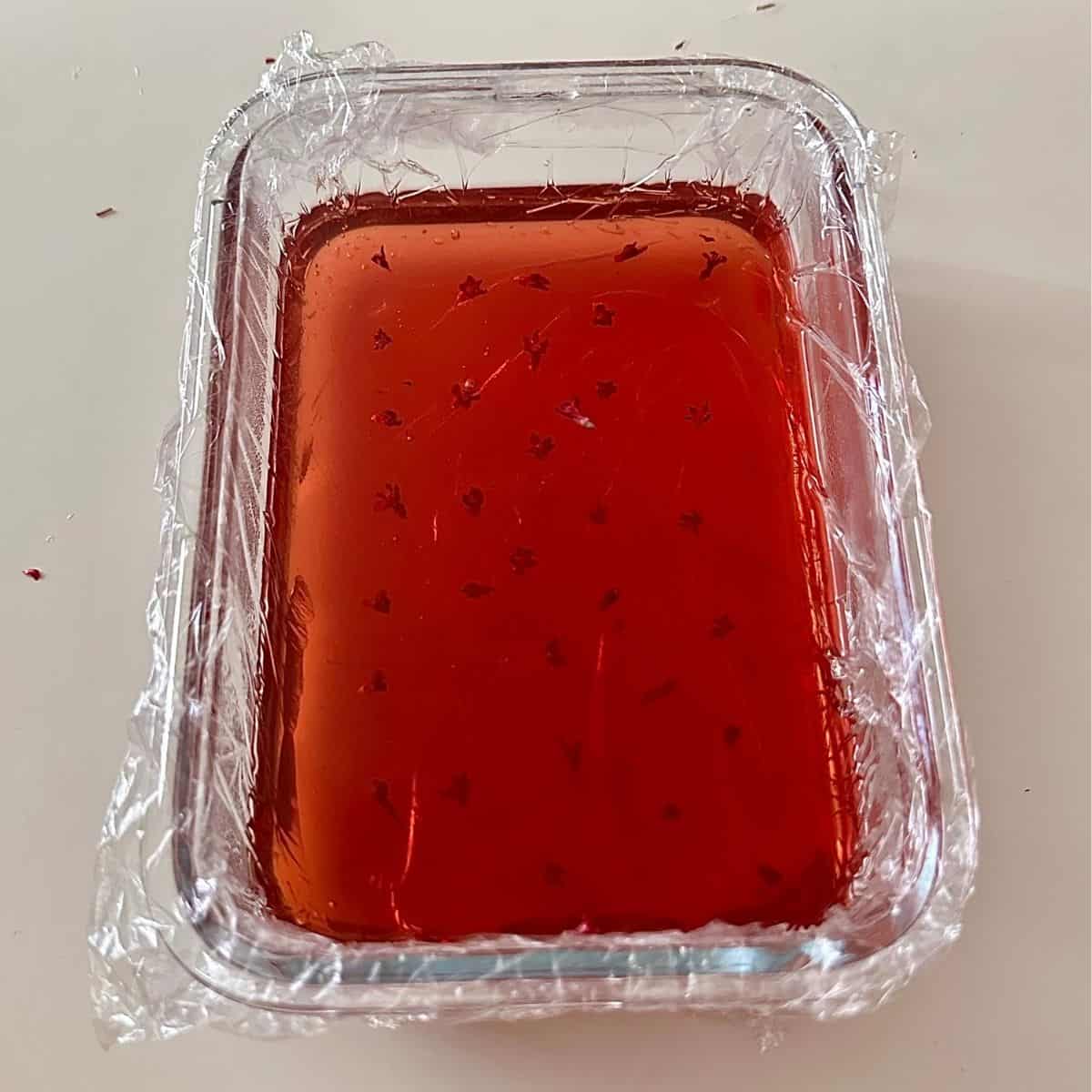 A glass dish lined with cling film, containing flowering current jelly dessert.