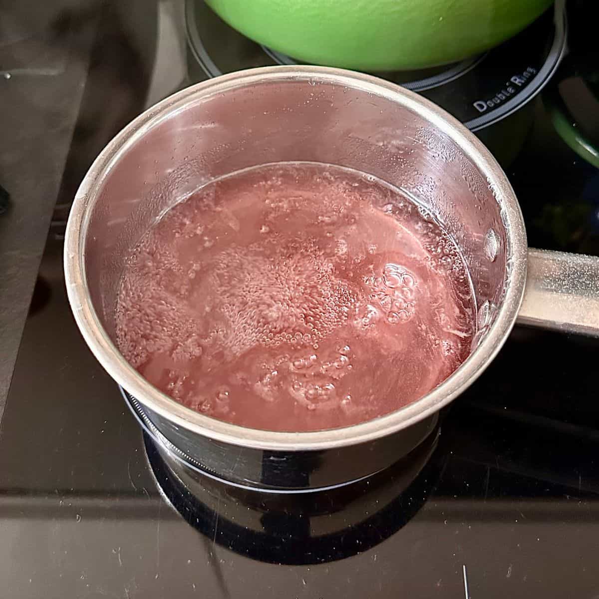A metal saucepan containing flowering current cordial and agar agar at a boil. For flowering current jelly dessert.