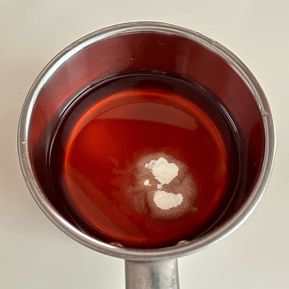 A metal saucepan containing flowering current cordial, chambord raspberry liqueur and agar agar for flowering current jelly dessert.