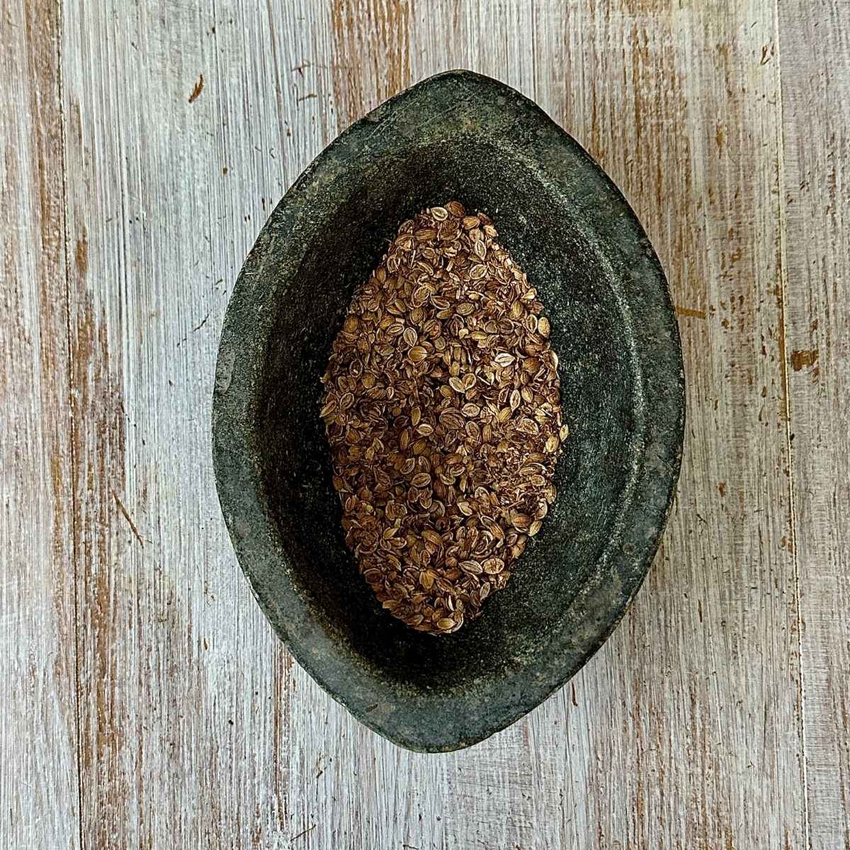 A pestle containing coriander seeds that have been slightly crushed for the super seed mix recipe.