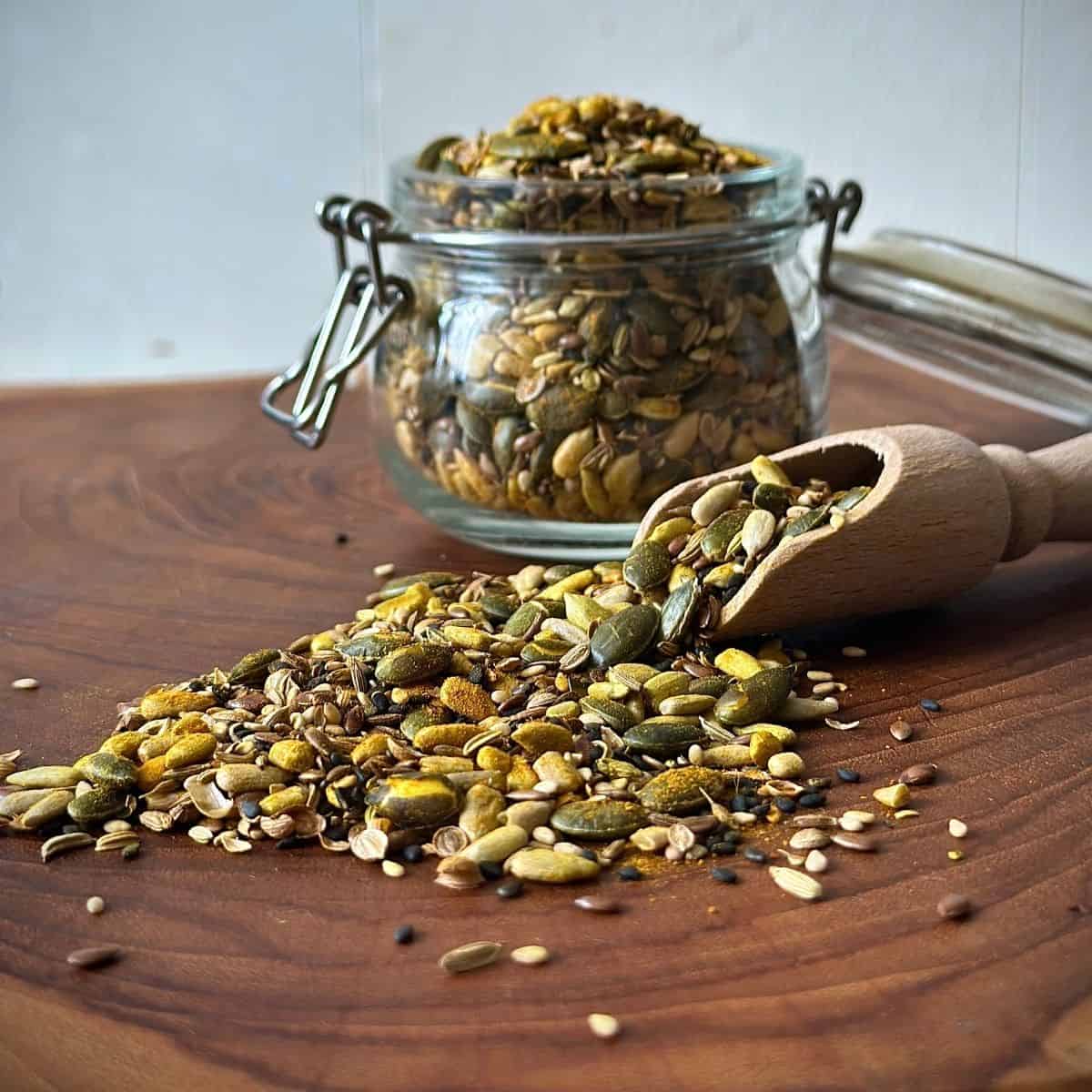 Super seed mix spread on a wooden chopping board, spilling from a rustic wooden spoon. A jar of the mix sits in the background.