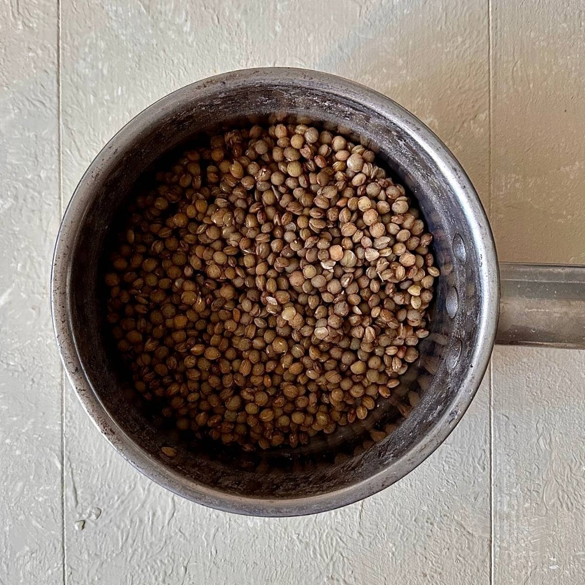 A steel saucepan containing green lentils in water for Camargue red rice, lentil and feta salad.