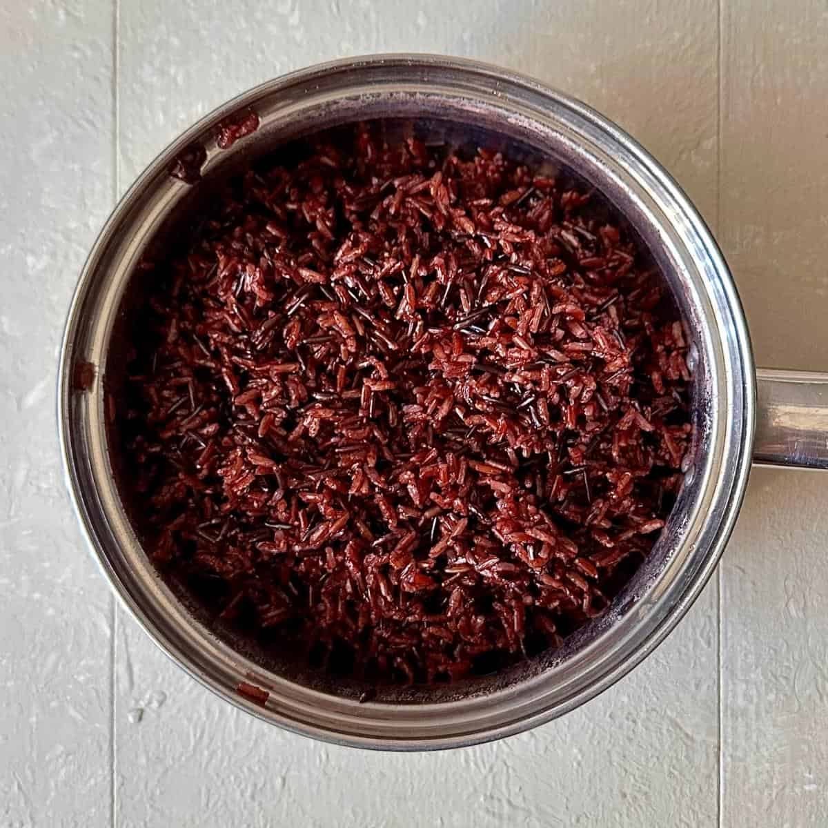 A steel saucepan containing Camargue red rice in water for Camargue red rice, lentil and feta salad.