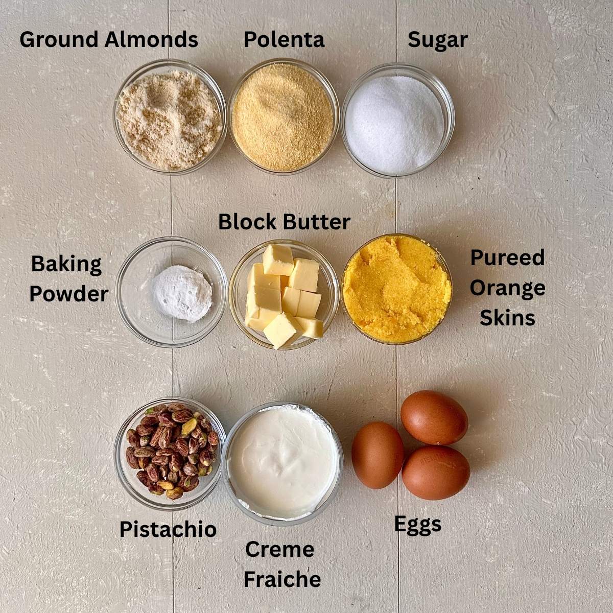 Ingredients for orange polenta cake in small glass dishes. The ingredients are annotated.