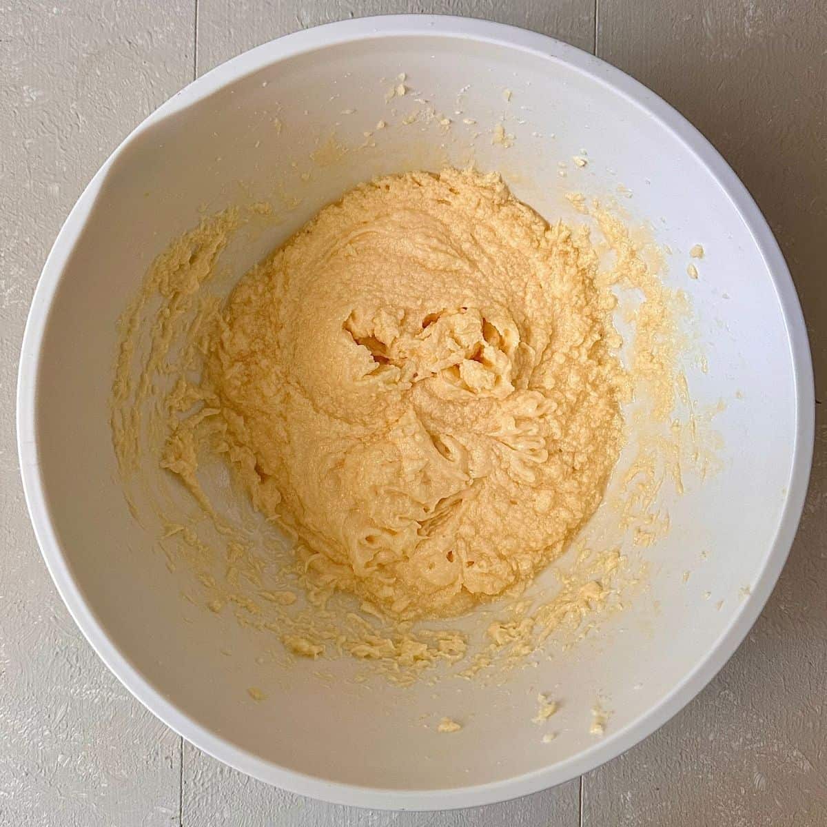 A mixing bowl contains batter for orange polenta cake. Batter stage is sugar and butter with eggs added and whisked together.