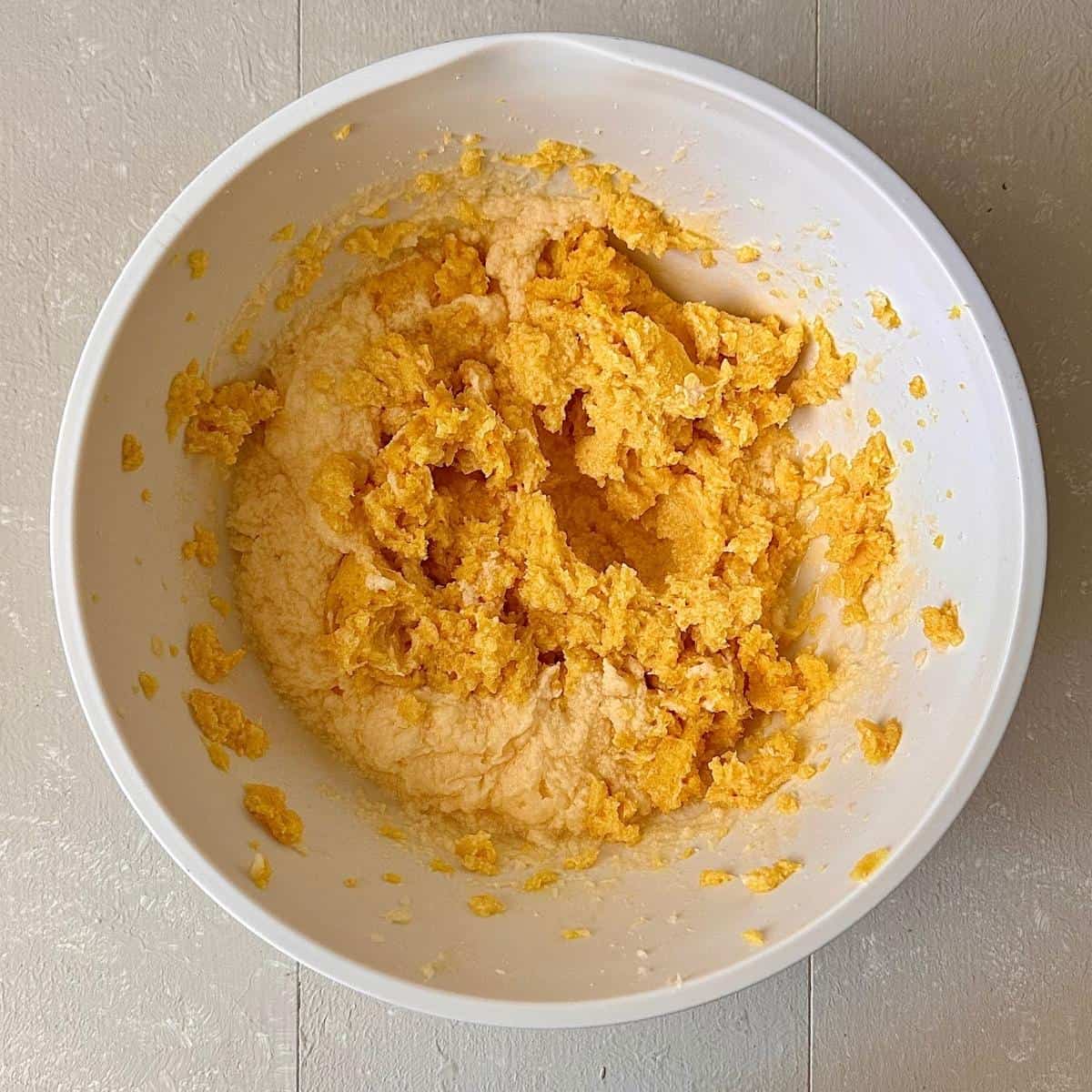 A mixing bowl containing batter for an orange polenta cake. Blended orange peel has been added to whisked butter, sugar and eggs.