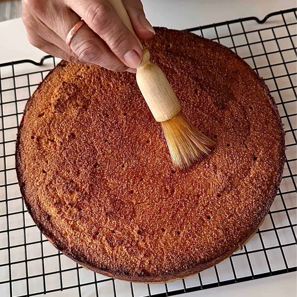 A baked orange polenta cake on a wire rack being brushed with watered down honey.