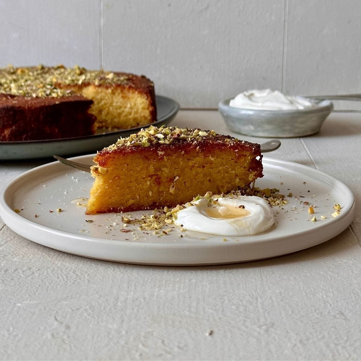 Slice of orange almond polenta cake served with crème fraîche, honey and chopped pistachios.