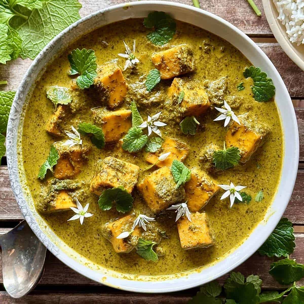 A bowl of wild garlic curry and paneer, garnished with ground ivy leaves and wild garlic flowers.