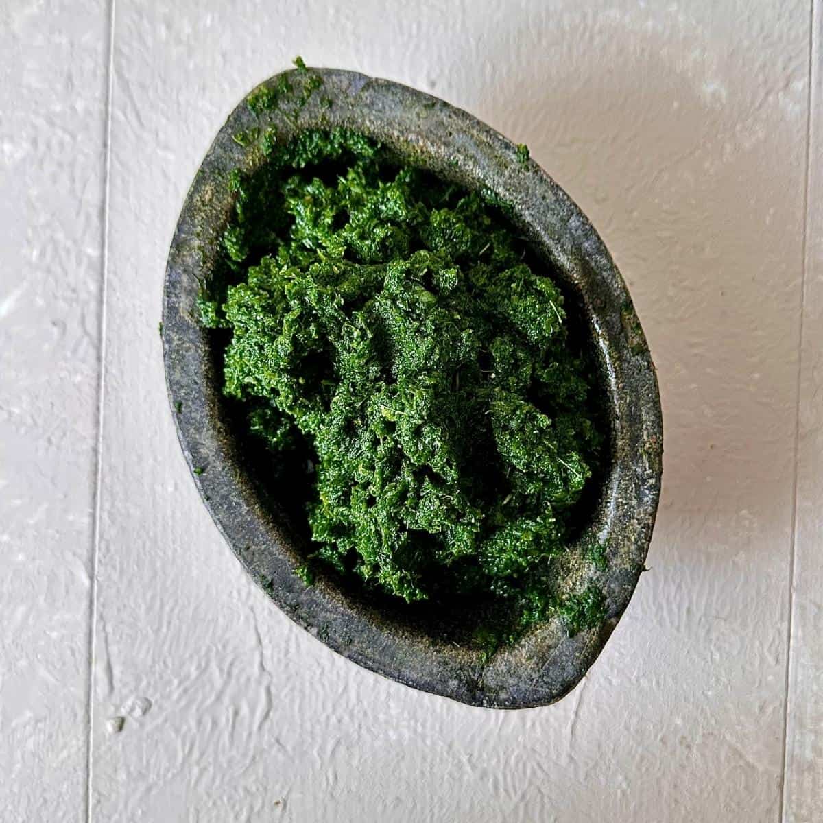 A stone pestle containing rough green paste consisting of ground wild garlic, garlic mustard, ground ivy, onion, garlic, ginger and lime leaves.