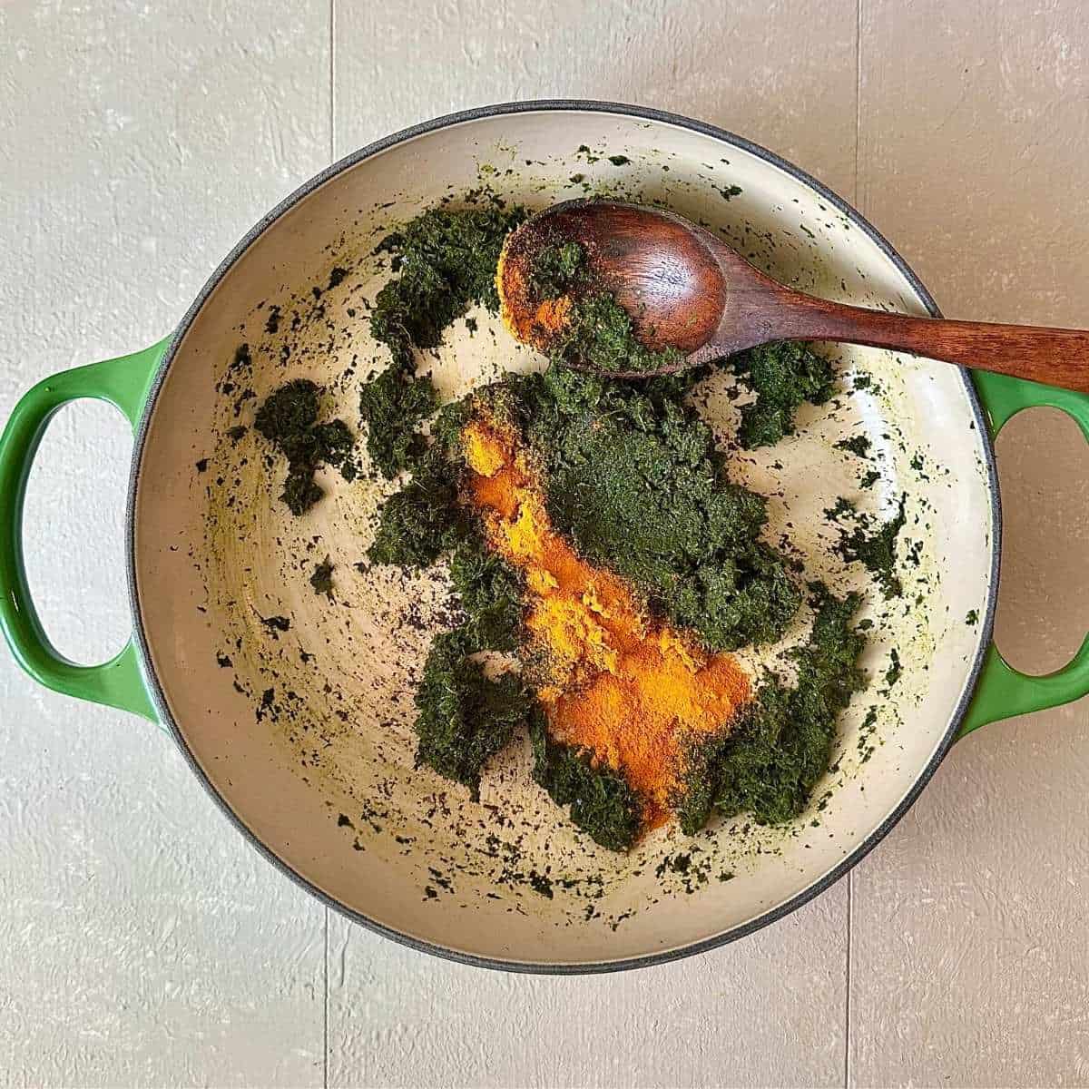 A large green casserole containing a rough paste of ground wild garlic, garlic mustard, ground ivy, onion, ginger and lime leaves with turmeric, for wild garlic curry.