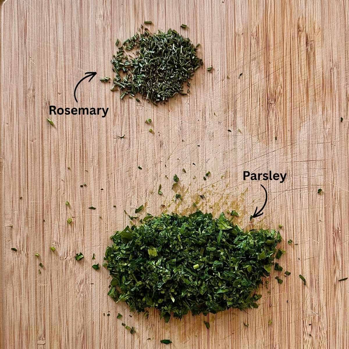 Finely chopped rosemary and roughly chopped parsley on a chopping board.