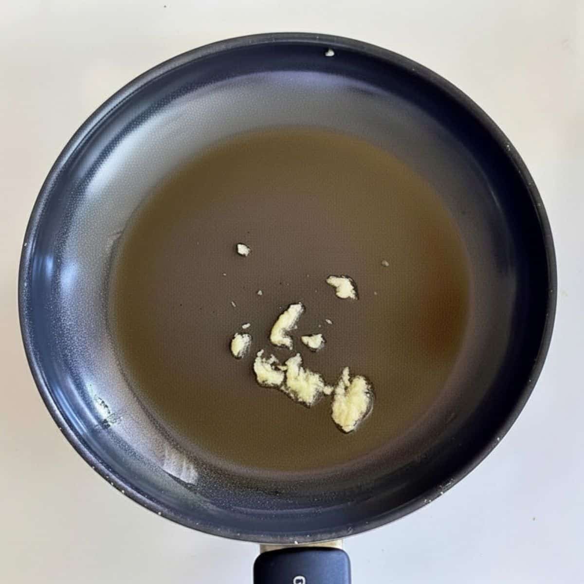 A frying pan containing grated garlic, frying, for Pangrattato crispy Italian breadcrumbs recipe.