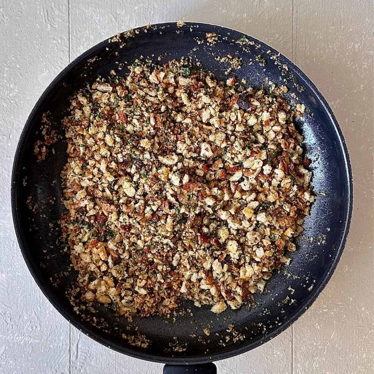 A frying pan containing fried sourdough breadcrumbs with rosemary and parsley for Pangrattato Crispy Italian Breadcrumbs.